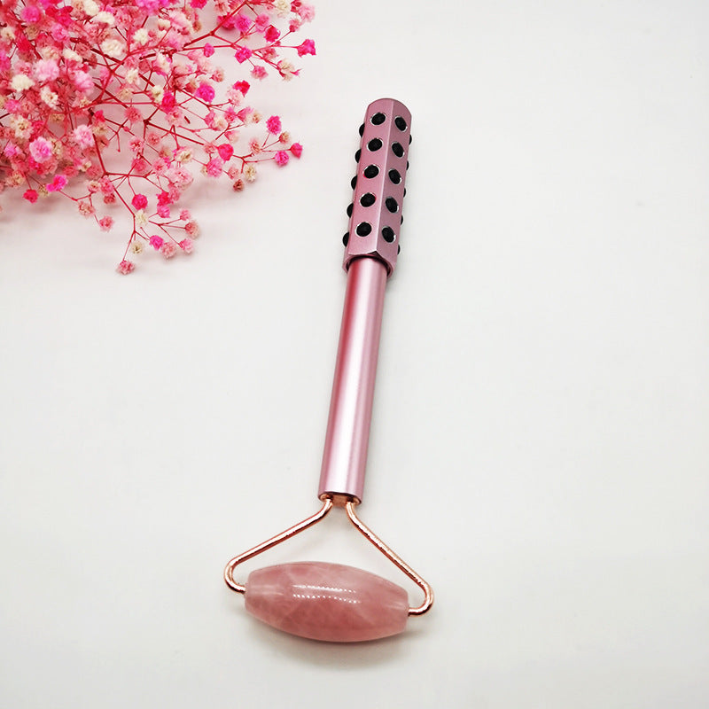 Pink facial roller with textured handle on a white background with pink flowers.