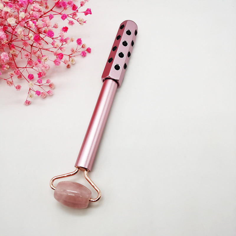 Pink facial roller with polka dot design on a light background with pink flowers.