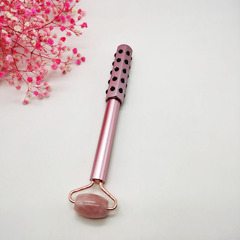 Pink facial roller with rose quartz stone on a light background with pink flowers.