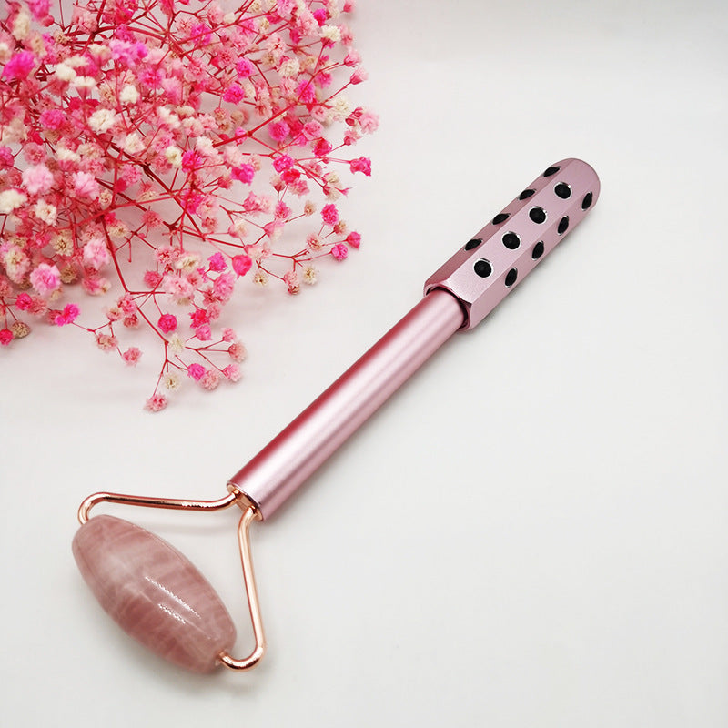 Rose gold facial roller with pink stone on a white background with pink flowers.