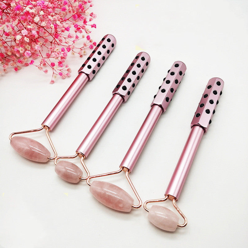 Set of pink facial rollers with rose quartz stones on a white background with pink flowers.