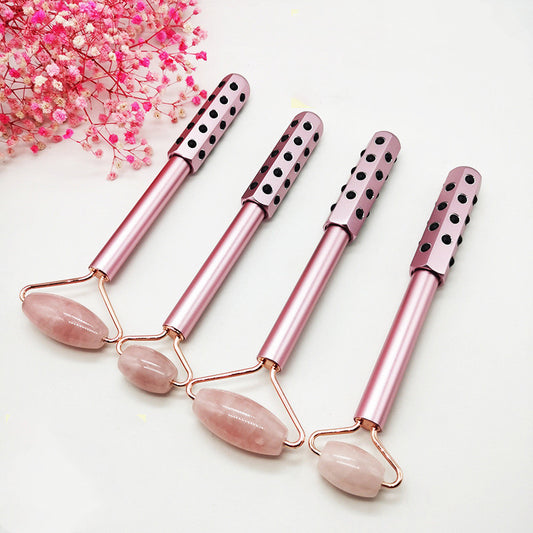 Set of pink facial rollers with rose quartz stones on a white background with pink flowers.