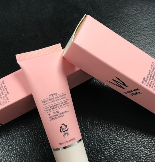 Pink cosmetic tube and packaging on a black textured surface